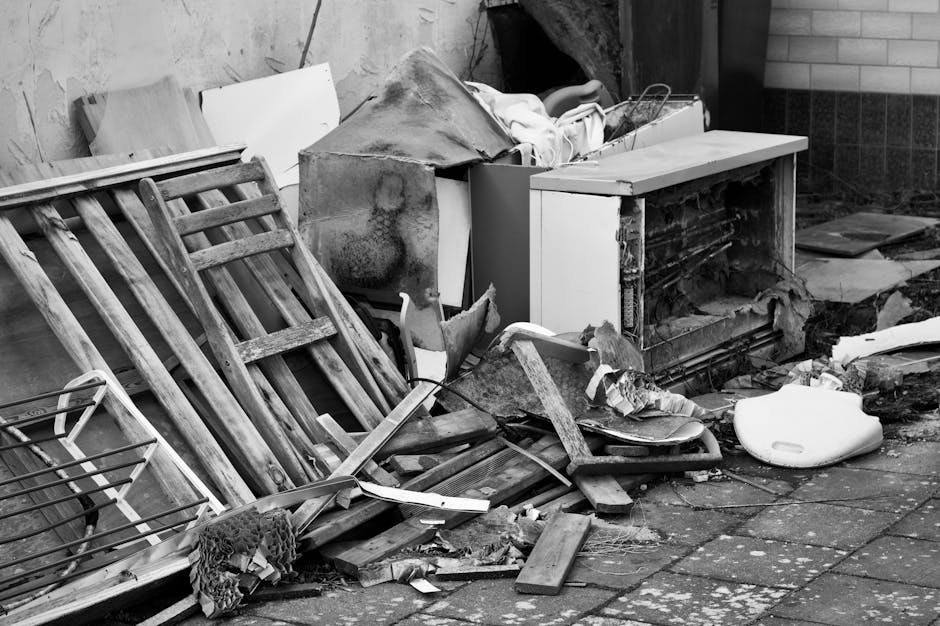 A pile of discarded wooden furniture, including a broken bed frame and slatted headboard, along with other debris such as pieces of broken wood, a white plastic container, and a damaged appliance, all